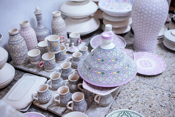 Colorful ceramic pottery collection featuring intricately designed cups, plates, and vases arranged on a textured surface, showcasing craftsmanship and artistic detail