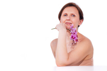 Woman with short hair, holding a purple orchid flower near her face, gazes thoughtfully into the distance, showcasing beauty and serenity in a minimalist setting with copy space