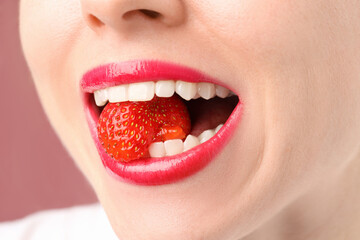 Woman with beautiful lips makeup and strawberry on dusty pink background, closeup