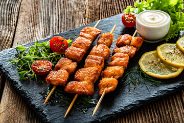Fried salmon skewers with white dip on stone board on wooden table	