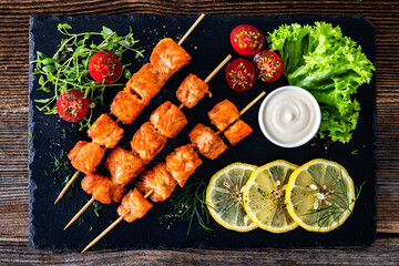 Fried salmon skewers with white dip on stone board on wooden table	