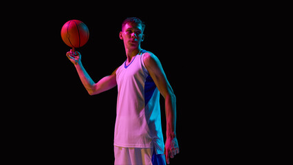 Basketball player in white jersey spinning ball on finger with focus under neon dramatic lighting. Concept of skill, creativity, show performance, sports lifestyle, and branding.