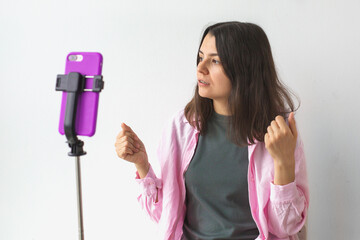 Woman in pink shirt speaking to smartphone on tripod, gesturing with hands and looking engaged, possibly recording vlog or video message, concept of communication