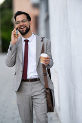 Businessman walking and talking on phone, holding coffee
