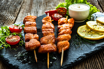 Fried salmon skewers with white dip on stone board on wooden table	