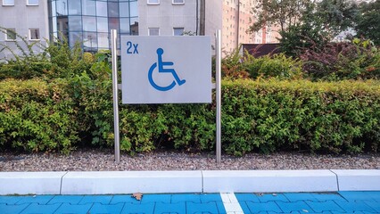 Accessible parking sign indicating two spaces reserved for disabled persons, with blue pavement and green hedge background
