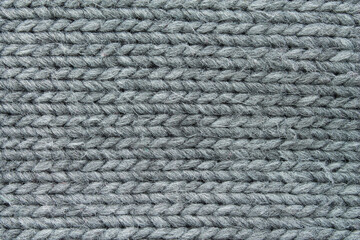 Gray knitted fabric texture background. Macro of a cozy handmade wool sweater with a stitch pattern. Concept of winter warmth, comfort, and hygge.