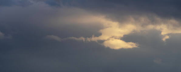 Large gray storm clouds with golden sun rays shining through them, creating a dramatic and gloomy atmosphere