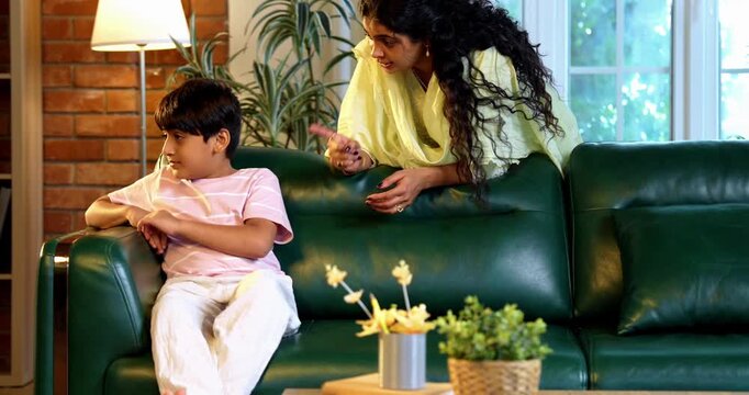Indian mother scolding son while sitting in modern home on sofa, teaching good habits, inculcating discipline, bonding in quality time, guiding child with love, parent child relationship indoors