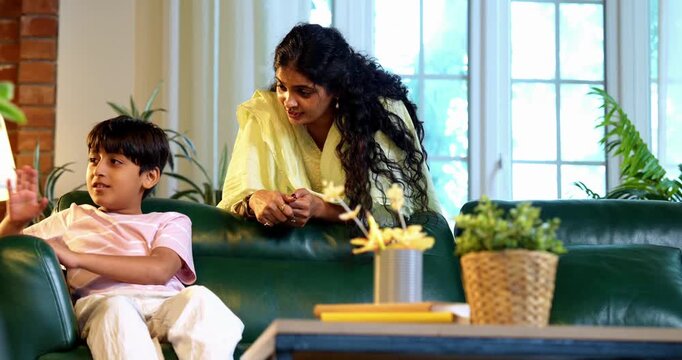 Indian mother scolding son while sitting in modern home on sofa, teaching good habits, inculcating discipline, bonding in quality time, guiding child with love, parent child relationship indoors