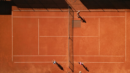 Three players practice drills on a sunlit clay court, showcasing dynamic movement and skill development in a professional sports setting, captured with an aerial shot.