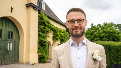 Yowung man in weddding suite waiting for future wife to arrive smiling in front of marriage vacinity