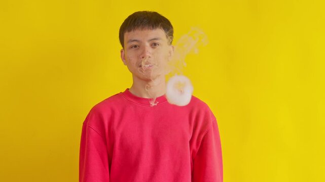 Excited Young asian man using vape device blowing o ring smoke isolated on yellow background