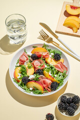 Fresh salad with peaches, arugula, feta, prosciutto and berries in a plate on a yellow background