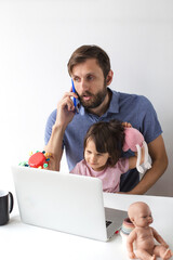 Father working from home with laptop and smartphone while holding his daughter on lap, surrounded by toys, multitasking parenting moment, concept of parenthood