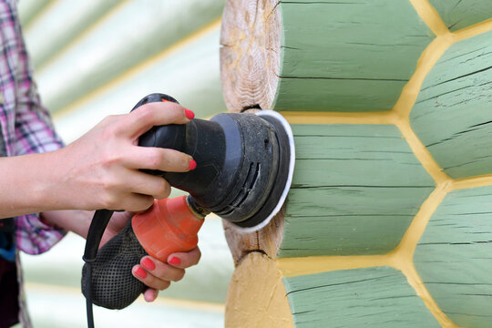 Close up of hand sanding wooden logs with electric sander during house renovation