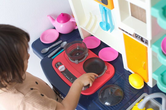 Child playing at toy kitchen stove with utensils, plates and cookware, engaging in imaginative pretend cooking activity, concept of childhood