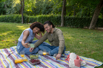 Interracial couple having fun taking selfie at picnic in park