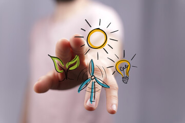 Conceptual hand interacting with digital icons: green leaf, sun, wind turbine, and light bulb. Symbolizes sustainable energy, environmental care
