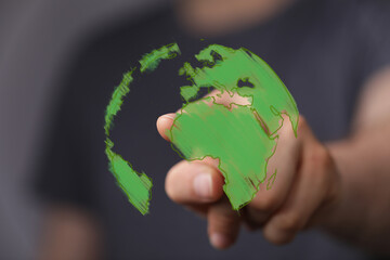 A human hand reaches out to a vibrant green digital globe, representing ecological awareness,...