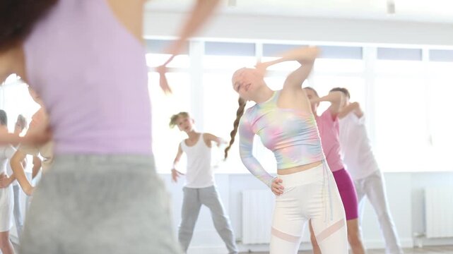 Girl teen performs modern dances repeats movements of unrecognizable teacher together with friends during lesson at choreographic school. Hobbies, active pastime