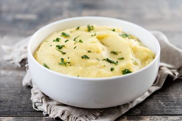 Mashed potatoes in white bowl on rustic wooden table