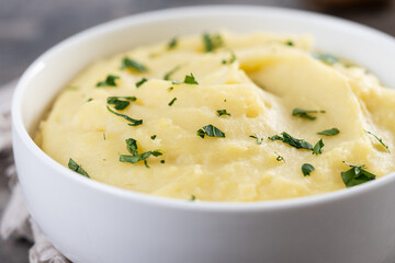 Mashed potatoes in white bowl on rustic wooden table. Close up