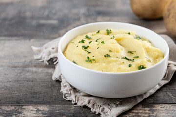 Mashed potatoes in white bowl on rustic wooden table. Copy space