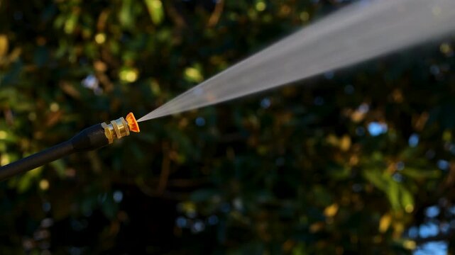 Power washer with yellow tip sprays high powered water jet with trees in background