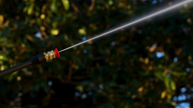 Power washer with red tip sprays high powered water jet with trees in background