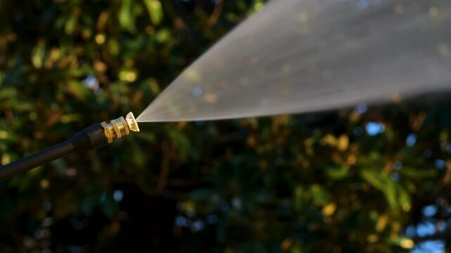 Power washer with white tip sprays high powered water jet with trees in background