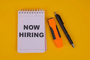 Now Hiring Text On Notebook With Pen And Highlighter Over Yellow Background