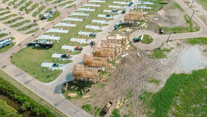 Circular street in RV trailer park and vacation rental community with timber stilt houses under construction with lumber, dumpster, green telescopic handler machines near Bolivar Peninsula, Texas