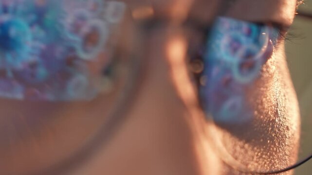 A person wearing glasses works on a laptop, with glowing reflections of viruses or bacteria in the lenses, symbolizing research, technology, health and broader conceptual ideas of science and society.