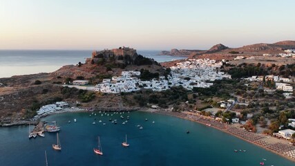 Explore breathtaking Lindos in Rodos, Greece from above showcasing stunning coastline, historic architecture, and vibrant waters in the sunset glow