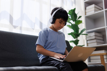 Asian boy using laptop wearing headphones at home
