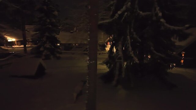 Aerial tracking shot low in middle of snowy trees and cabins, night in Finland