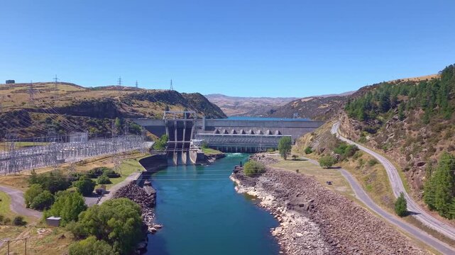 Low reverse aerial rising above the Clutha River to reveal the full Roxburgh hydro dam and scenic Roxburgh Lake in Central Otago, New Zealand.