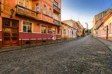 uzhhorod, ukraine - 11 jun, 2017: narrow street of old town leads to square in empty historic center at sunrise. beautiful architecture of uzhhorod in morning light under blue sky. scenic downtown