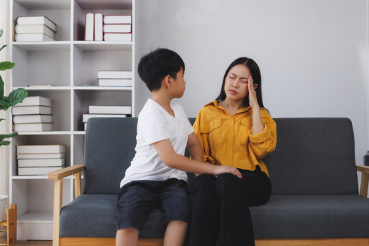 Asian mother suffering from headache at home with son comforting her