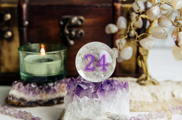 Number twenty-four gemstone sphere or crystal ball known as crystallum orbis. Natural clear quartz ball on stand on crystal geode home, candle burning. Predictions concept.