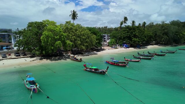 Drone pushes back over turquoise shallows as longtail boats line the shore at Rawai Beach