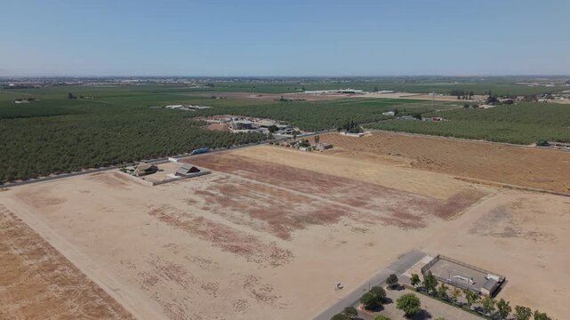 Aerial side shot showing farmland, road with traffic, houses, and open fields in Ripon California.