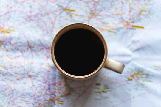 A cup of coffee on a map. Coffee cup placed on a world map. Dark coffee in a mug on a travel map. Coffee and map, perfect for travel planning. Adventure trip planning.