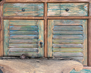View of rustic vintage credenza drawers cabinet with weathered wood panel and jalousie louvered door in shades of brown, blue, and yellow color. Traditional rural ethnic and retro furniture.