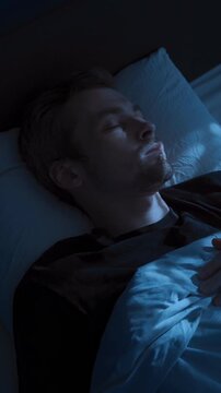 A young man wakes up tense and exhausted in bed at night, suffering from insomnia and a sleep disorder, covering his face with his hand. Sleep paralysis or nightmares