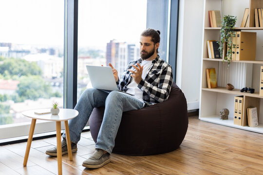 Middle-aged man with beard and laptop engaged in video call, sitting in cozy living room