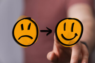 A hand interacts with a digital display showing a sad face transforming into a happy face,...