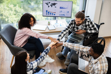 Group of four diverse colleagues in teamwork hand-stack gesture promoting unity and inclusion....