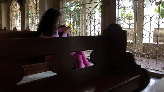 Young Asian teen girl is deeply focused on playing mobile games in the church hall, unaware of her surroundings.